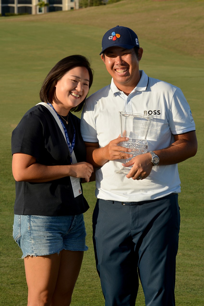 Byeong Hun An holds up the 2022 LECOM Suncoast Classic trophy and poses with his wife, Jamie Heejae An, after winning the tournament at 17 under par (65-66-67-69—267).