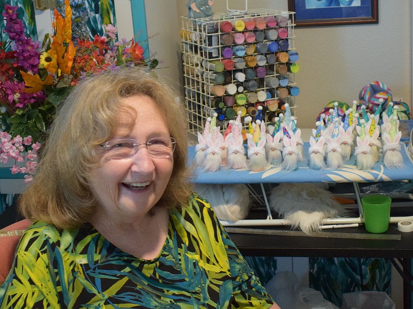 Linda McMillen sits in her home workshop with miniature gnomes, made out of champagne corks, behind her.