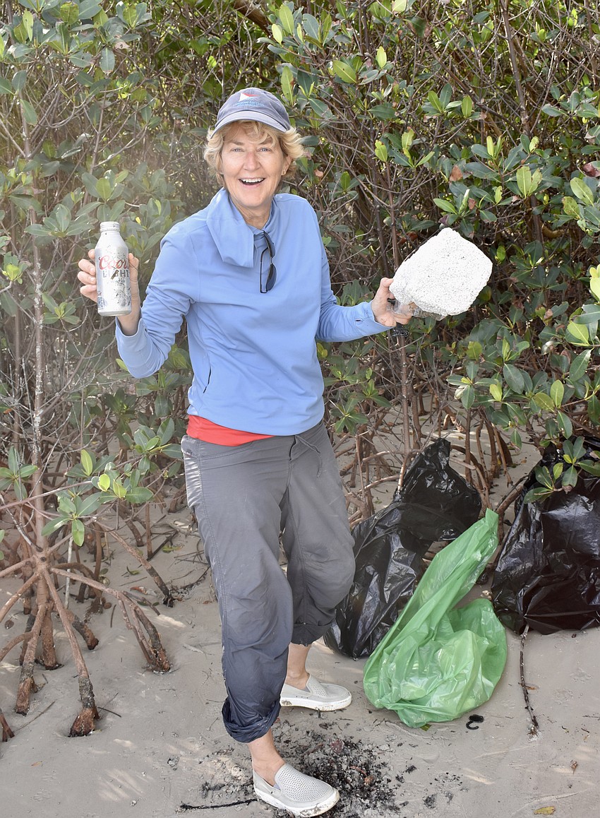 Maureen Merrigan steps from the mangroves with a discarded piece of  foam and a cast-aside can of unopened beer.