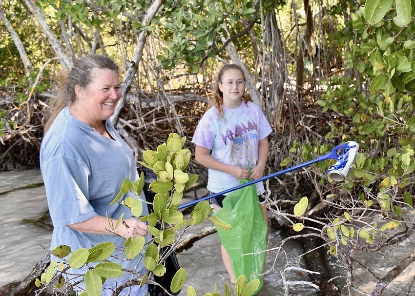 Susan Cranwell grips an empty beer can she found along the shoreline while working with Calynn Stewart.