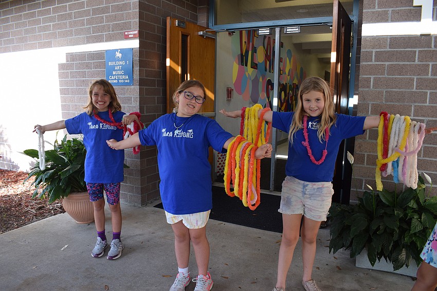 Third graders Savannah Grosso, Emily Whited and Gloriana Jobst offer leis to guests as they enter.