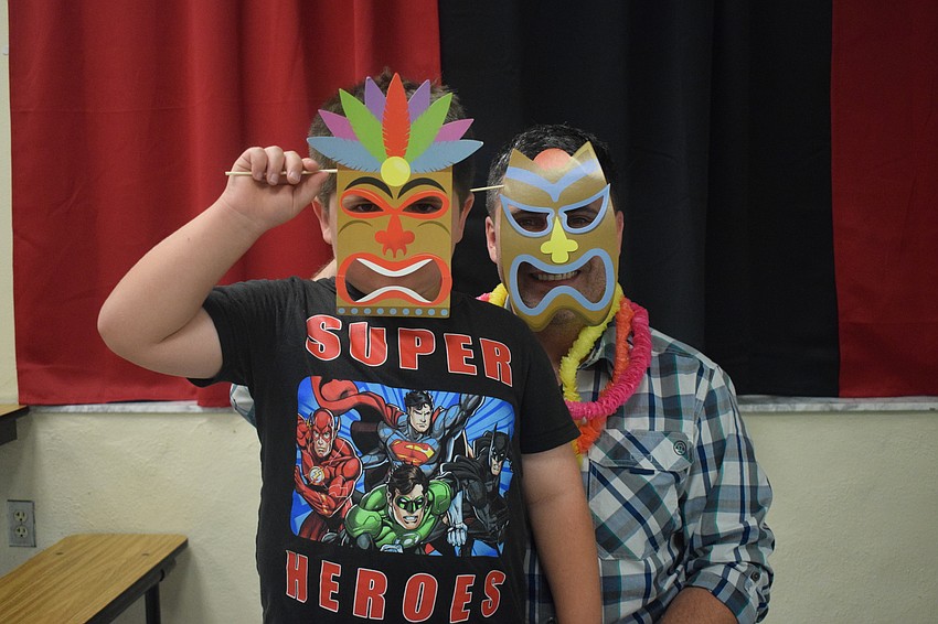 Kindergartner Emmett Johnson and his father, Dennis Johnson, wear tiki masks for the photo booth. Emmett Johnson looks forward to dancing with friends.