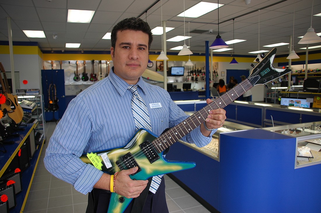 Photo by: Isaac Babcock - Sales associate Juan Hernandez shows off a guitar at a La Familia Pawn Shop in Orlando.