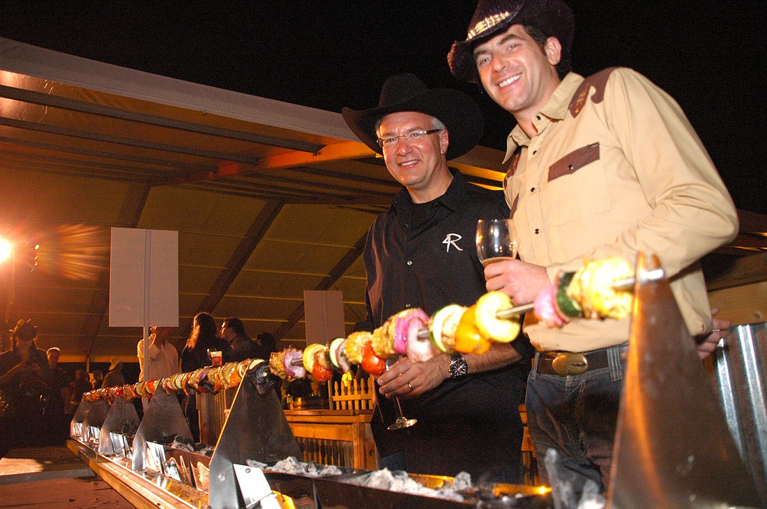 Photo by: Isaac Babcock - 4Rivers owner John Rivers and The Food Network's Adam Gertler stand behind a 30-foot-long skewer at the Cows 'n Cabs event Oct. 22, held in Winter Park to raise money for Coalition for the Homeless, Community Outreach and the...