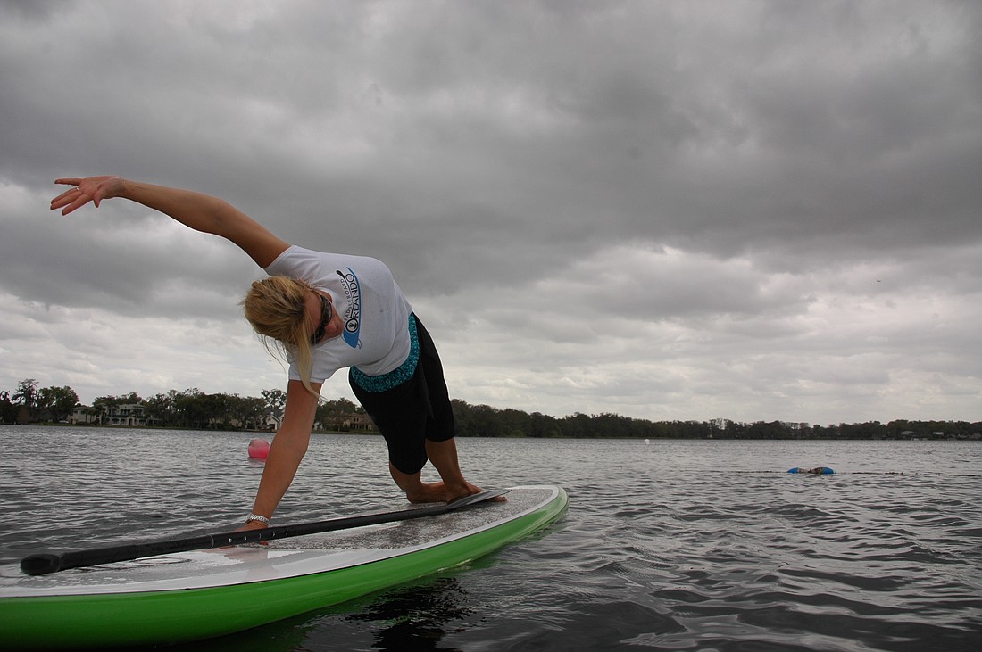 Photo by: Isaac Babcock - Kim DePasquale performs a yoga pose atop a paddle board on Lake Virginia in Winter Park as she instructs students in her stand up paddling yoga class, which helps students master balance.