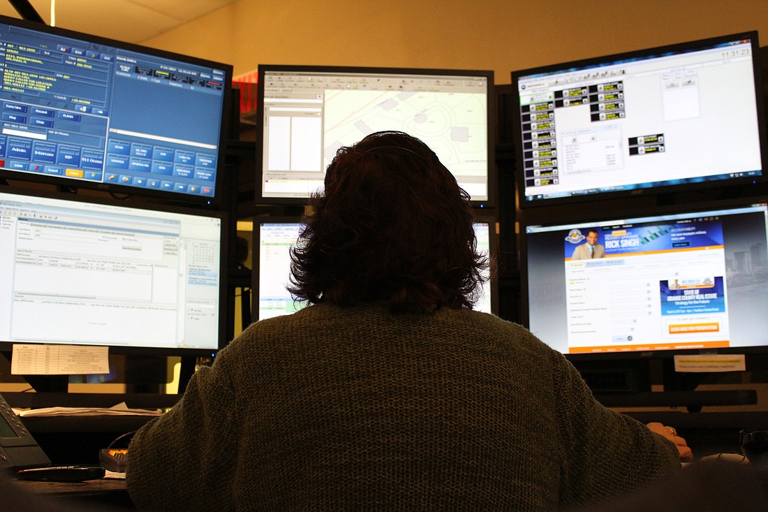 911 dispatcher Debra Duval handles a call while working in her height-adjustable desk in front of six computer screens in the WGPD call center.