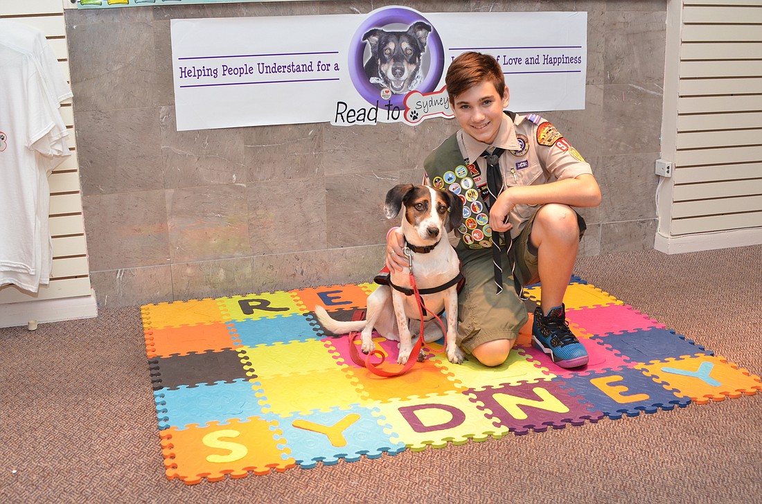 Eagle Scout candidate Elijah Kelly is providing books, tables and seating for the Read to Sydney program in the West Oaks Mall. With him is reading buddy Toby.