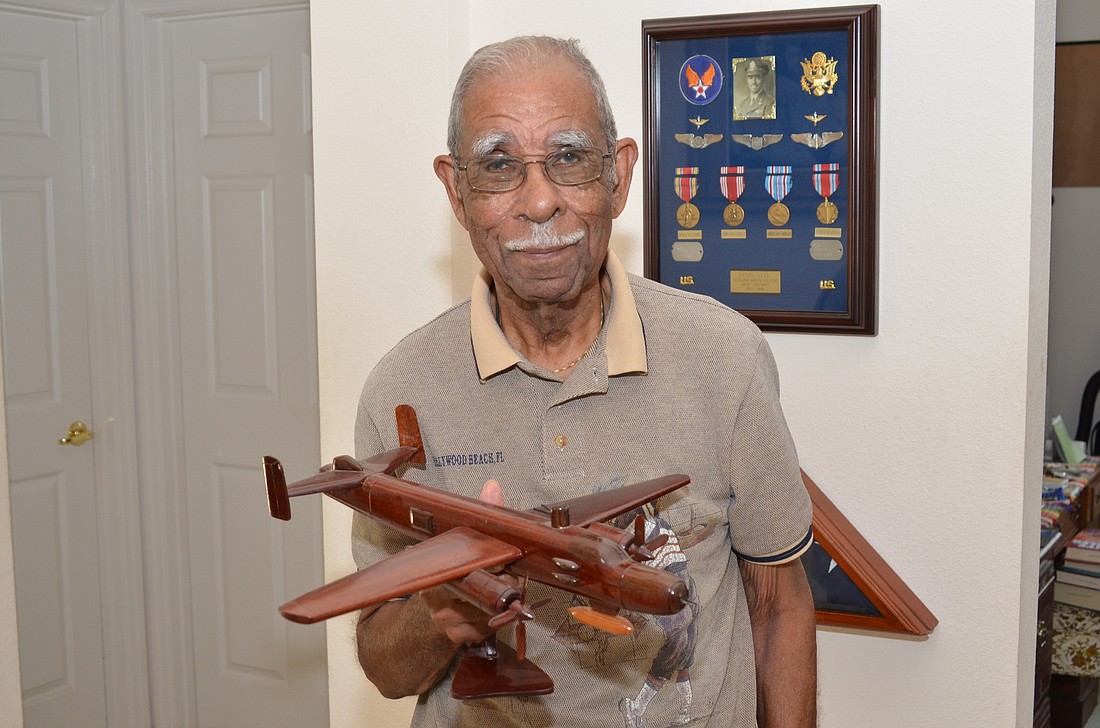 Daniel Keel holds a replica of the plane he trained on during World War II. On the wall beside him are the medals and the three sets of wings â€” pilot, navigator and bombardier â€” he received.
