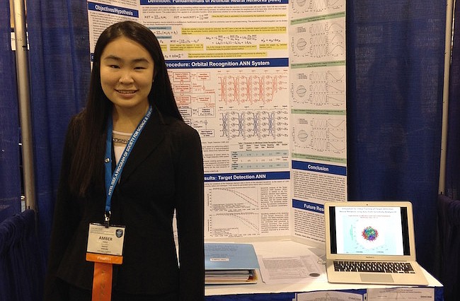 Photo by: Kristen Fiore - Amber Yang stands in front of her science project which uses computer modeling and data to help satellites avoid space debris. The project was chosen for the Regeneron Science Talent Search.