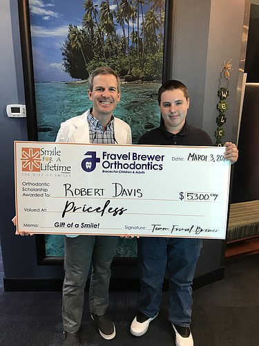 Dr. Breck Brewer hands a patient an oversized check to represent the orthodontic scholarship he received.
