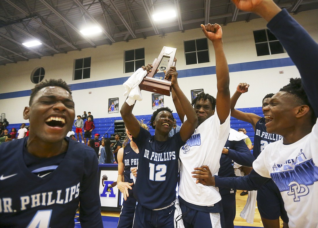 Abdoulaye Thiam, center, held up the district trophy as he celebrates with teammates following Dr. Phillips basketballâ€™s 58-53 win over Ocoee in the Class 7A, District 3 championship.