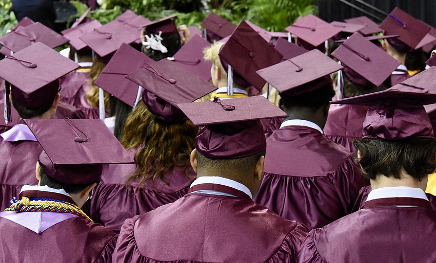 Seated graduates who have already received their diplomas watch their classmates proceed across the stage.