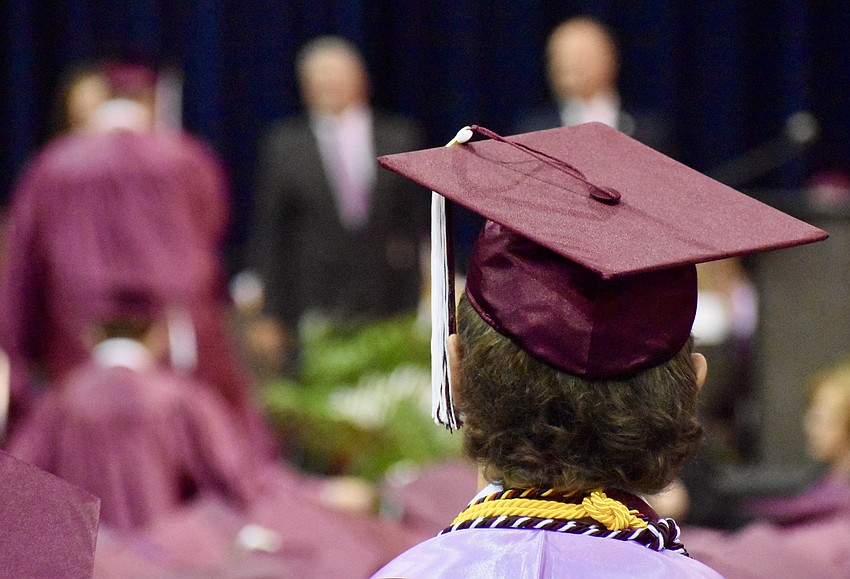 Graduates proceed forward to receive their diplomas while their classmates watch.