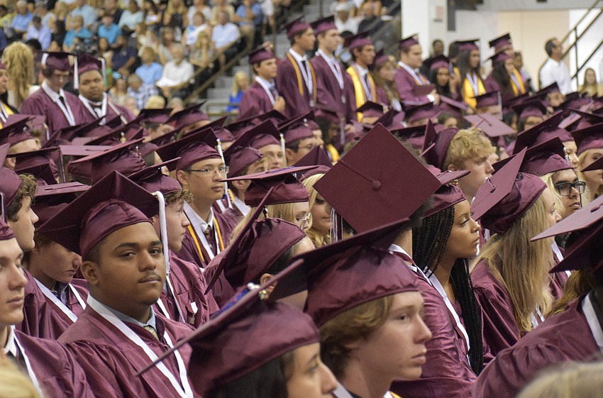 Graduates proceed forward to receive their diplomas while their classmates watch.
