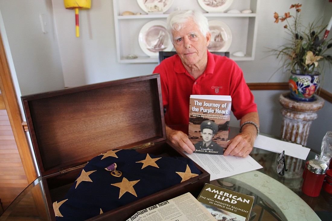 Bob Baumer holds up a copy of his book, "The Journey of the Purple Heart," next to his uncle's purple heart and flag. Photo by Jarleene Almenas