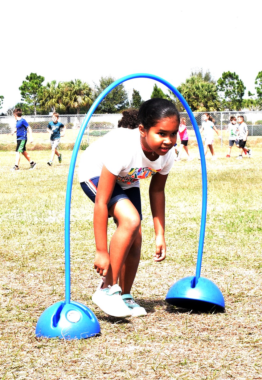 Second grader Victoria Nunez runs under a hoop to get through an obstacle course.