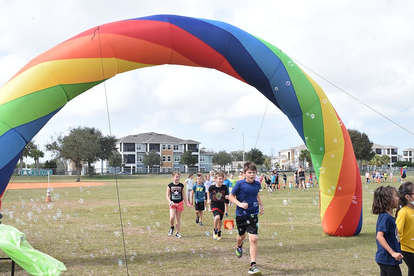 Second graders run under the rainbow bridge completing another lap of the walkathon.