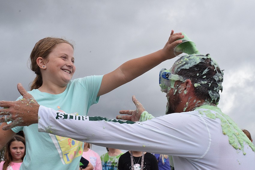 Third grader Emma Jackson pours slime over Principal Todd Richardson's head as he reaches out to her.