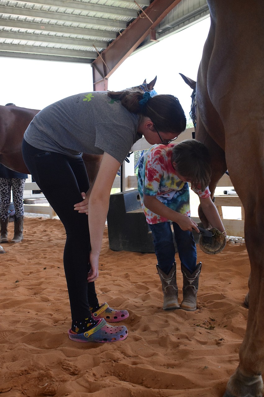 Lily Moore, a camp counselor, helps 9-year-old Lucius Rowell clean Cherokee's hooves.