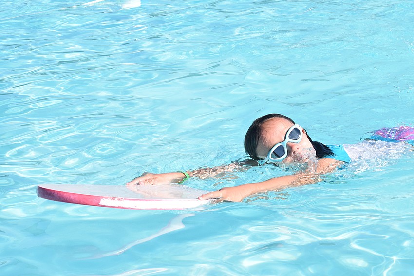 Teia Smith uses a kick-board to help her practice swimming during aquatics camp.