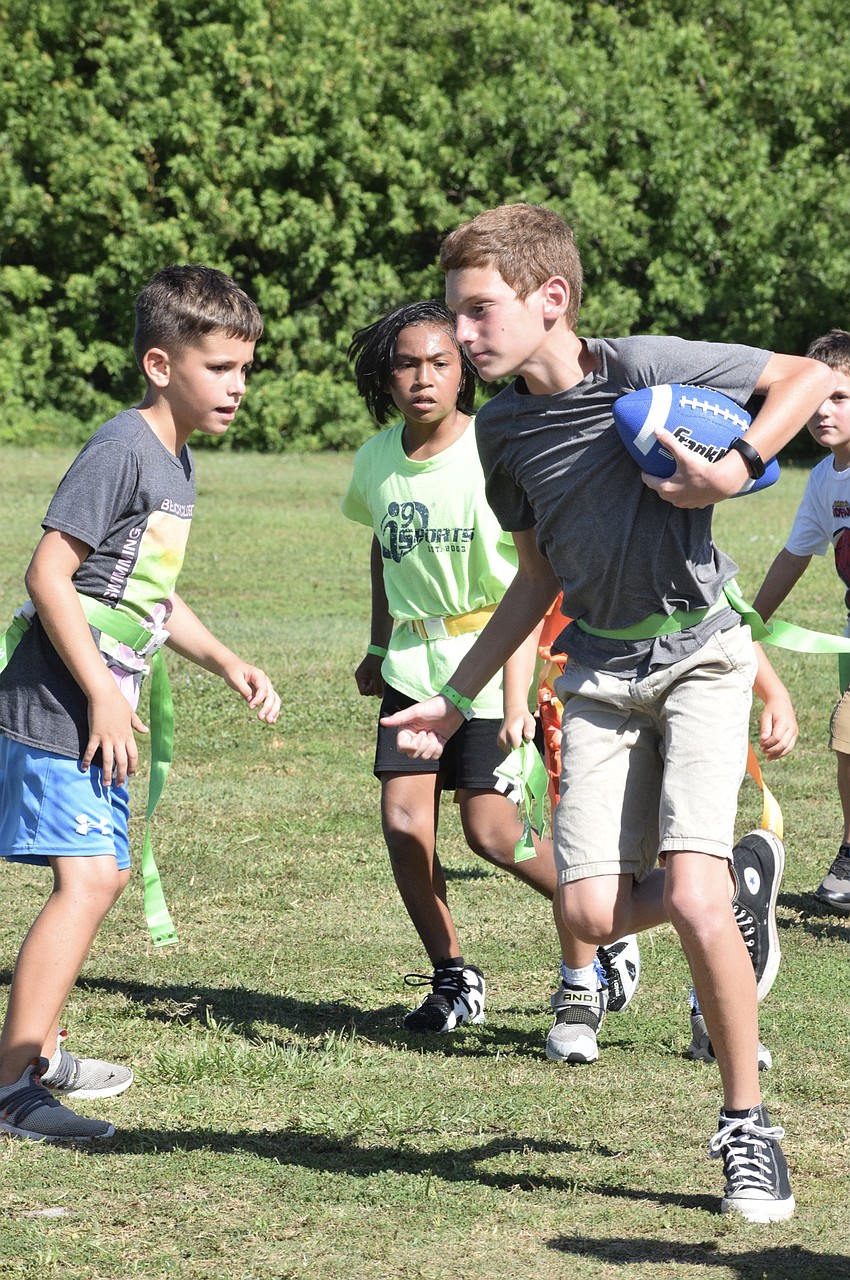Jackson Smith and Mateo Petrelli watch as Tristan McGlaughlin carries the ball toward the middle of the field in flag football.