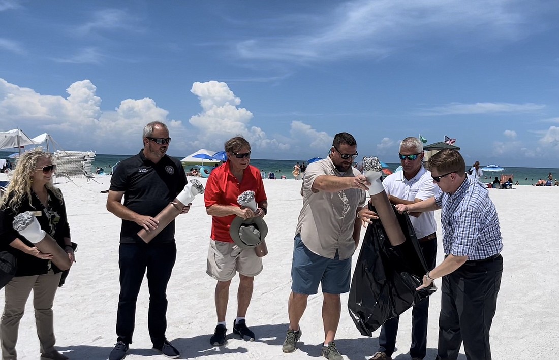 Participants in Friday&#39;s beach smoking ban event ceremoniously place giant cigarette butts in a trash bag, illustrating the state&#39;s enabling legislation allowing localities to prohibit smoking on the beach. (Courtesy photo)