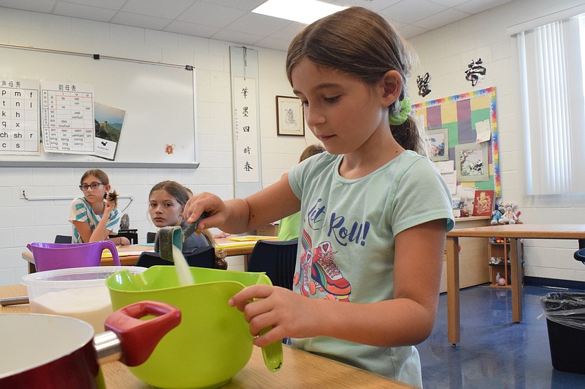 Violet Reinhartz, who is 7 years old, measures sugar and puts it in her group's mixture to create pretzel dough.