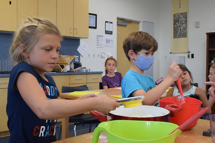 Hailey Royce, who is 6, measures and adds flour to her mixture while Joshua Rodriguez, who is 6, stirs his. Each member of the group took turns adding ingredients to their pretzel dough.