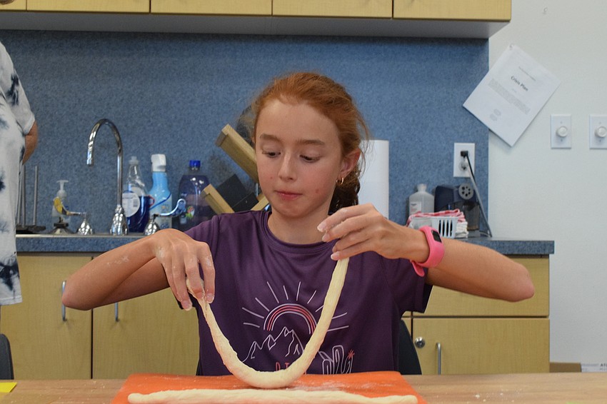 Julia Oliveira, who is 10, picks up her dough to try to twist it into a pretzel shape. It took her a few tries before she was able to make the traditional pretzel shape.