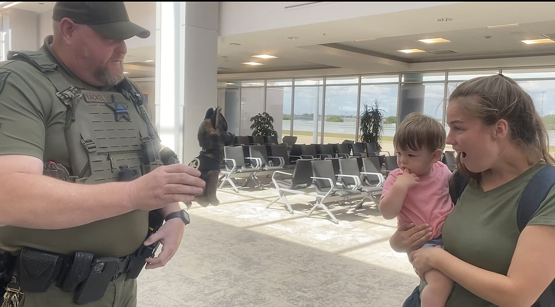 VSO Sr. Deputy Brad Yackel surprises passengers with a plush toy of his K-9. Screenshot courtesy of DBIA's video