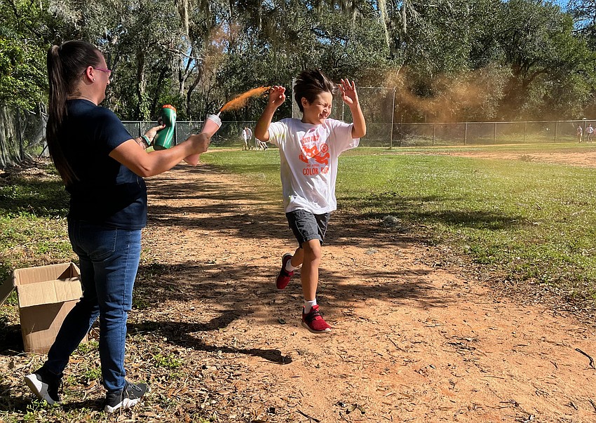 Volunteer Lauren Mancusi sprays fifth grader Jaiden Vega with orange powder as part of the color run.