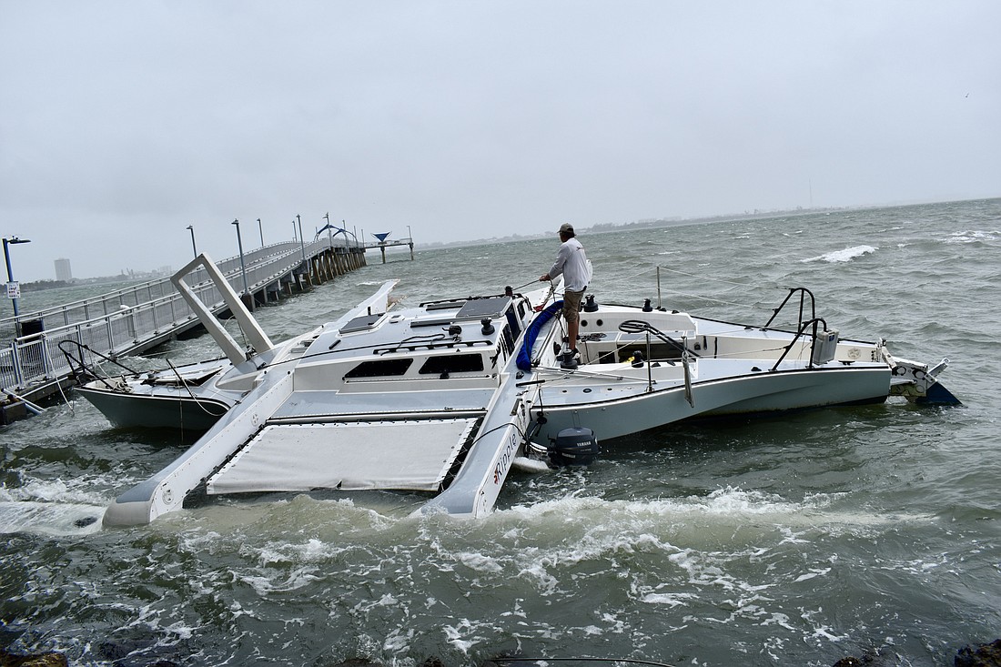 A man aboard a trimaran sailboat that was driven against the seawall at Hart&#39;s Landing works with a crew on shore to secure the craft with lines. (Eric Garwood)