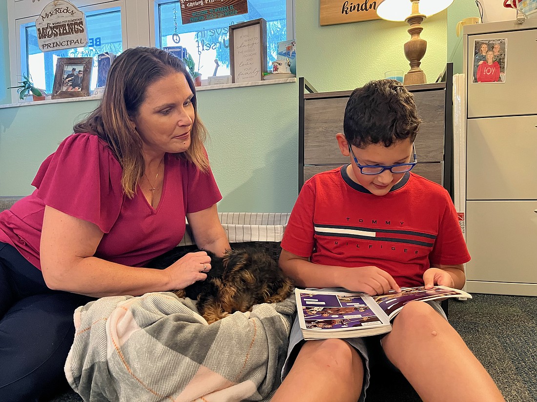 Principal Carol Ricks listens and pets Ruby as fourth grader Christopher Tovar reads "I Survived." Tovar was able to participate in Reading to Ruby as a reward for having the most accelerated reader points in his class.