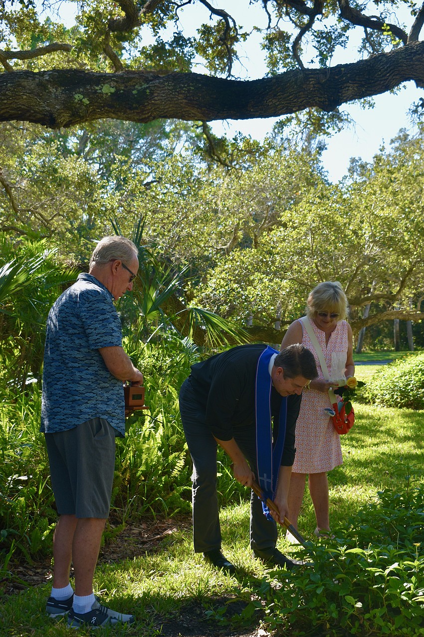 Jeff and Laurel Vaughn watch as Rev. David Marshall digs a hole for their dog Harvey's ashes.