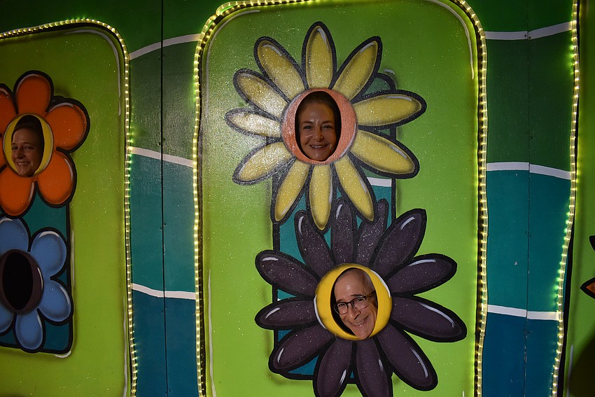 Emma Lyons, Lisa and Jeff Silvershein poke their heads through the billboard flowers.