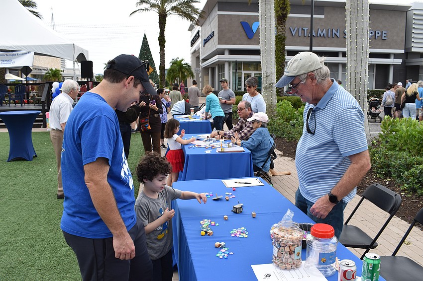 Lakewood Ranch's Andrew Bunin and 5-year-old Jacob Bunin visit a table staffed by Sarasota's Geoff Ingalls. Jacob tried to win a gemstone by spinning the dreidel.