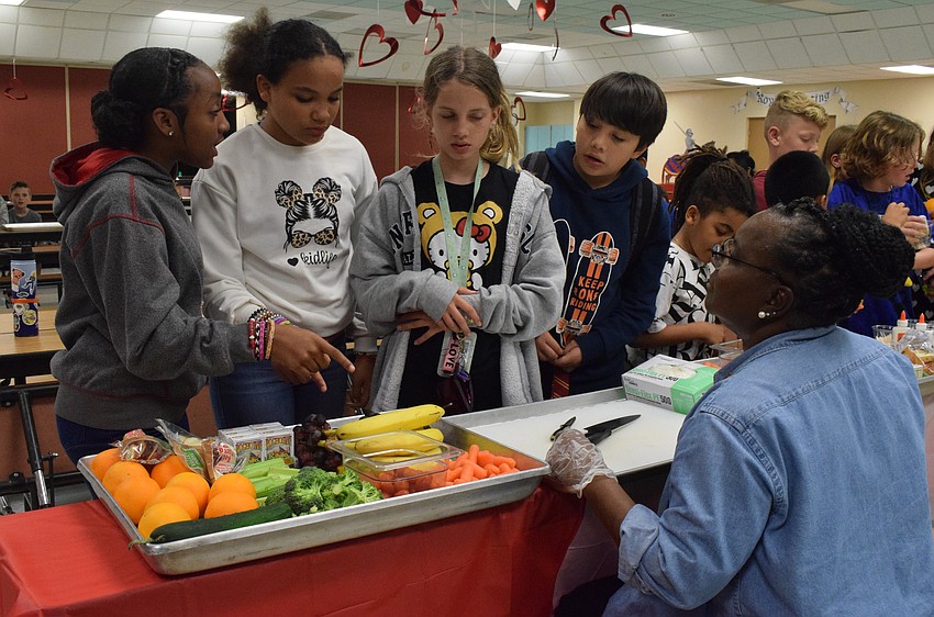 Fifth graders Dailaini Ward, Bella Randall, Zailee Segars-Lopez and Santaigo Olvera discuss what fruits and vegetables they want to use to create turtles while Laura Rowe, a cook at Tara Elementary School, waits to help cut fruits and vegetables for them.