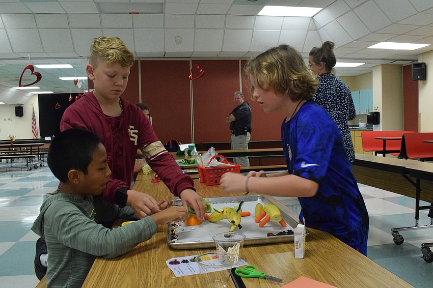Fourth graders Martin Torres, Wyeth Hudson and Archer Miles are hard at work putting together their display, which features a dolphin, panther and turtle made of various fruits and vegetables.