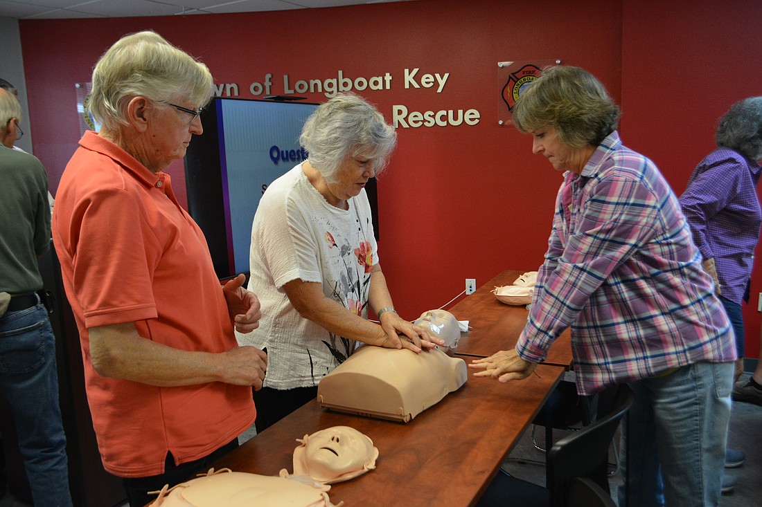 Pat Watral shows Pam Toft how to hold her arm while performing CPR. Toft's husband, Graham, watches.