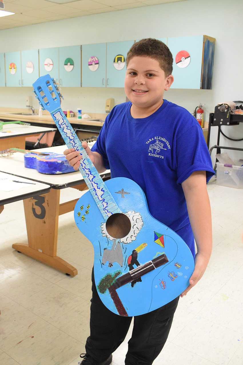 Fifth grader Kadem Spikes shows off the guitar he painted during Art Club. He says the guitar has a sky theme complete with a flying squirrel, toucan, kite, butterfly and airplane.