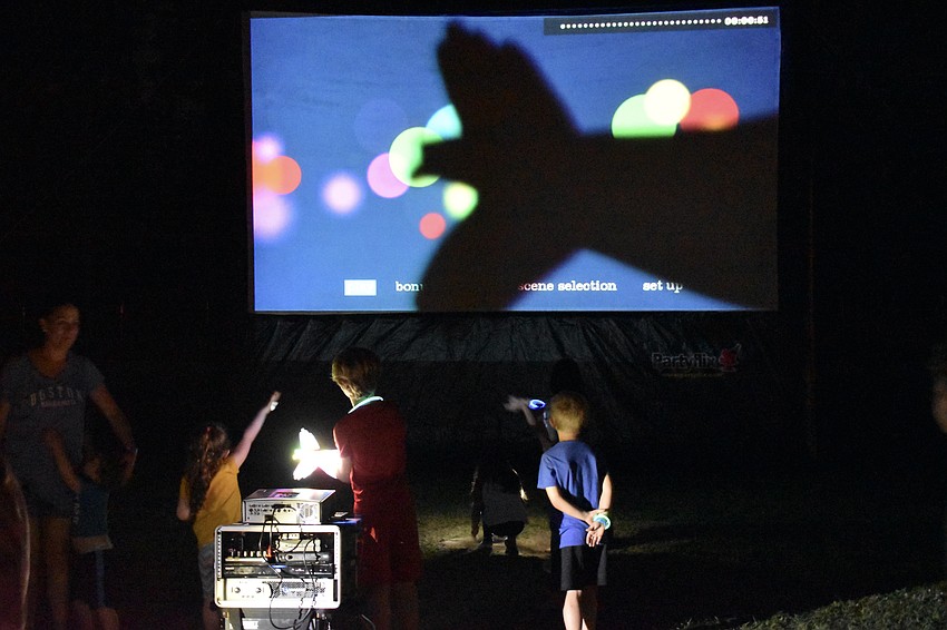 8-year-old Elijah Barshinger, 8, demonstrates his skill at making shadow puppets before the start of the movie screening during the Community Campout.
