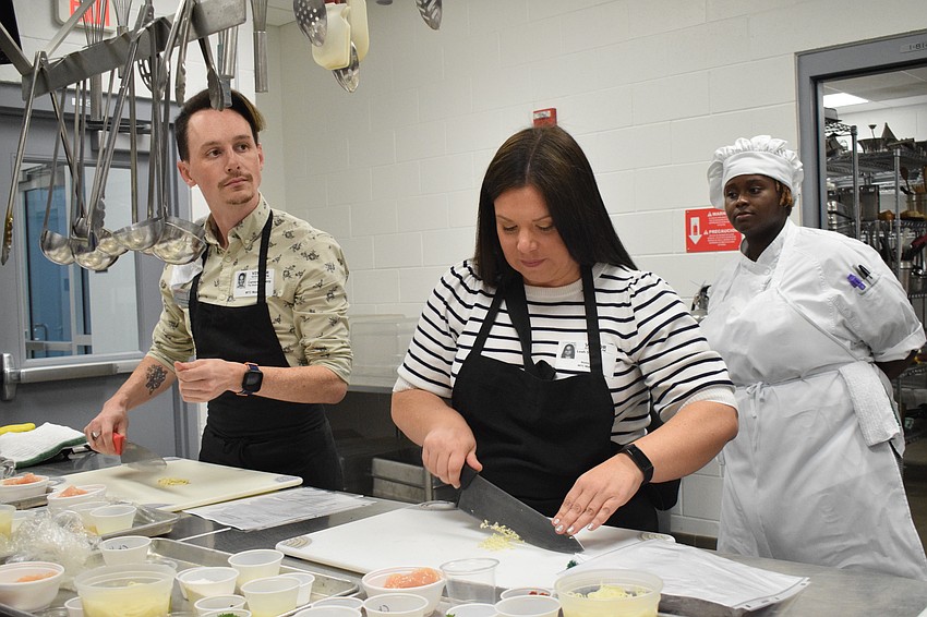 Lakewood Ranch Young Leaders Alliance members Cameron Thorp and Leah Stuart cut ingredients under the watch of Manatee Technical College culinary student Shamya Andrews.