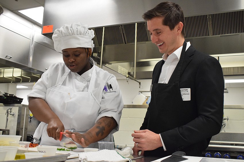 Manatee Technical College culinary student Shamya Andrews shows Tieler Gittleman, the chair of the Lakewood Ranch Young Leaders Alliance, the finer points of using a knife.
