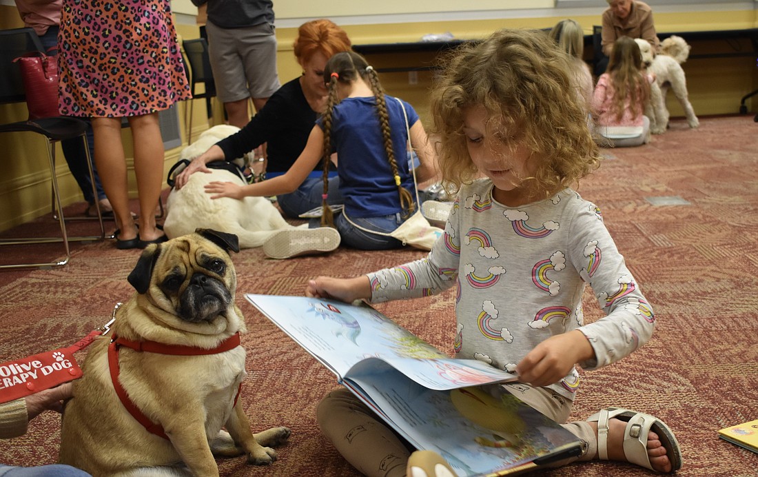 6-year-old Emilia Kalev reads to Olive, a pug who arrived with Joanne Long, a volunteer with The Bright and Beautiful Therapy Dogs.