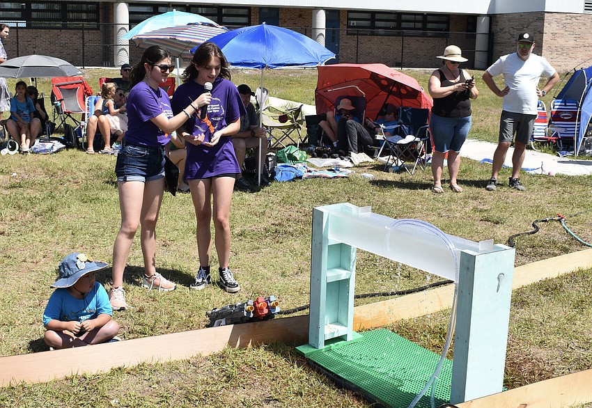High school volunteer Natalie Carrion asks fellow volunteer Hailie Palmer to describe how she built the waterfall in the obstacale course.