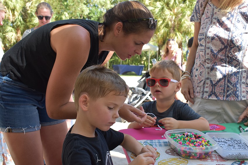 Shelbie Palmer helps 4-year-old Caleb Palmer and 3-year-old Owen Palmer create wristbands at the Girl Scouts station.