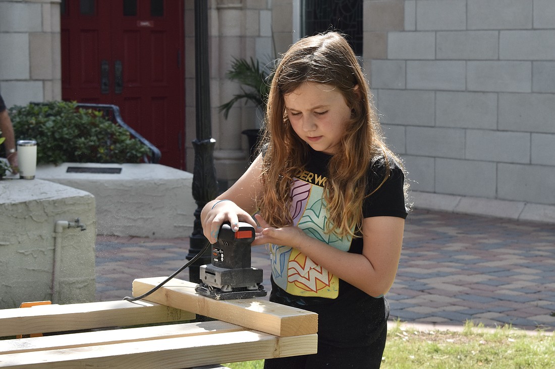 8-year-old Claire Bragg sands a piece of wood.