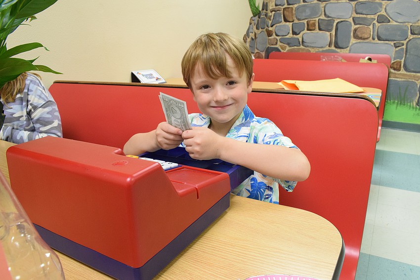 Kindergartner Logan Johnson is happy to be a cashier at the Banana Leaf Restaurant.