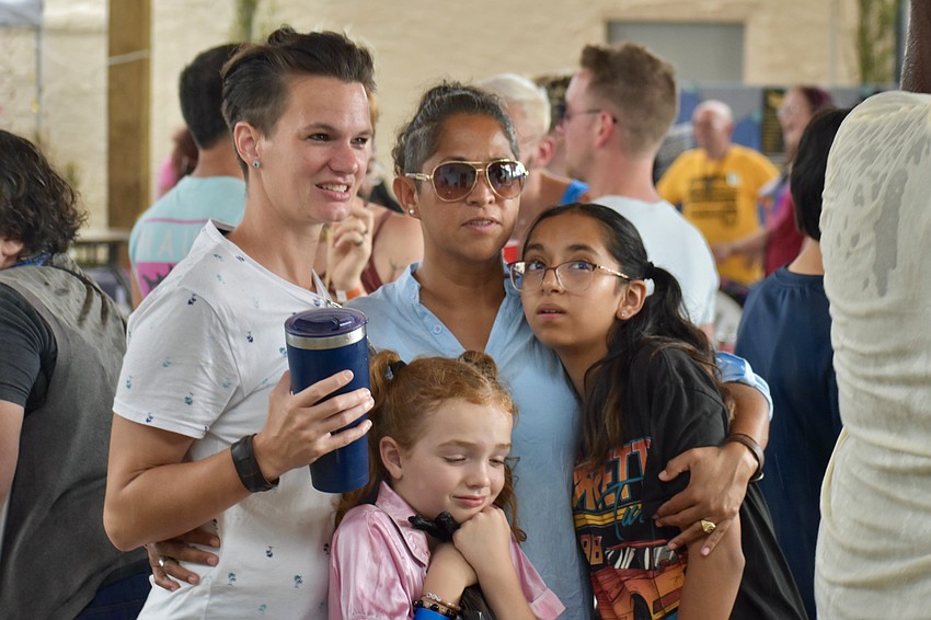 Julia Kaster, 8-year-old Olivia Kaster, Delia Diaz, and 12-year-old Keana Mercado huddle together under the main tent as a downpour of rain begins.