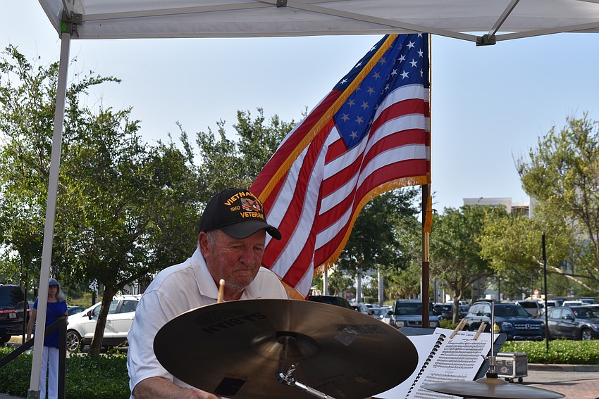 Drew Trapani of the Lakewood Ranch Wind Ensemble performs on the drums with Old Glory blowing in the background.